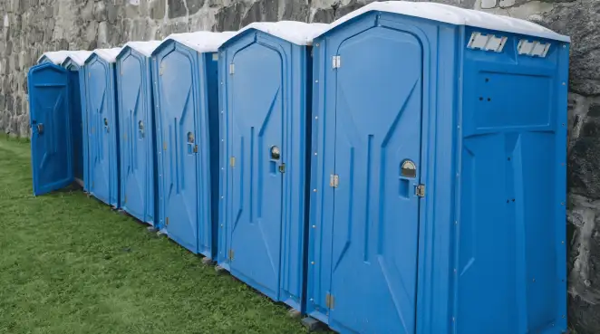 Row of blue portable toilets lined up on grass against a stone wall for event sanitation in Tacoma, WA