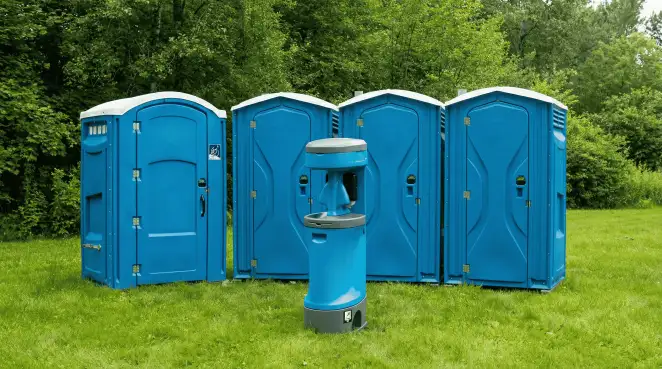 Four blue portable toilets and a matching hand washing station on grass near trees, a common sight at local outdoor events in Tacoma, WA