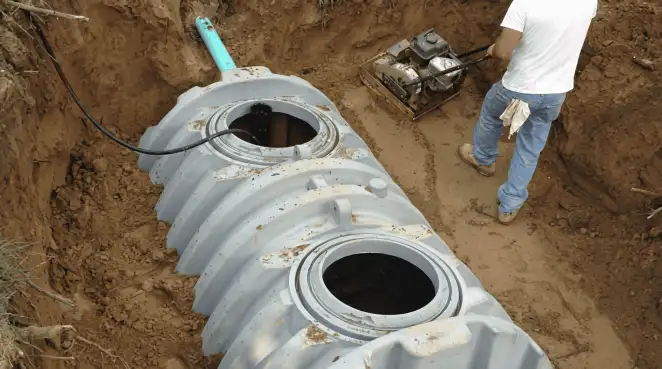 Septic tank installation showing a technician compacting soil around a new poly septic tank in an excavation pit in Tacoma, WA